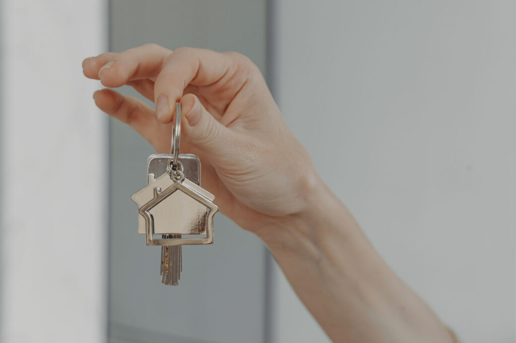 woman holding house shaped keychain, selective focuse on female hand with key from new home